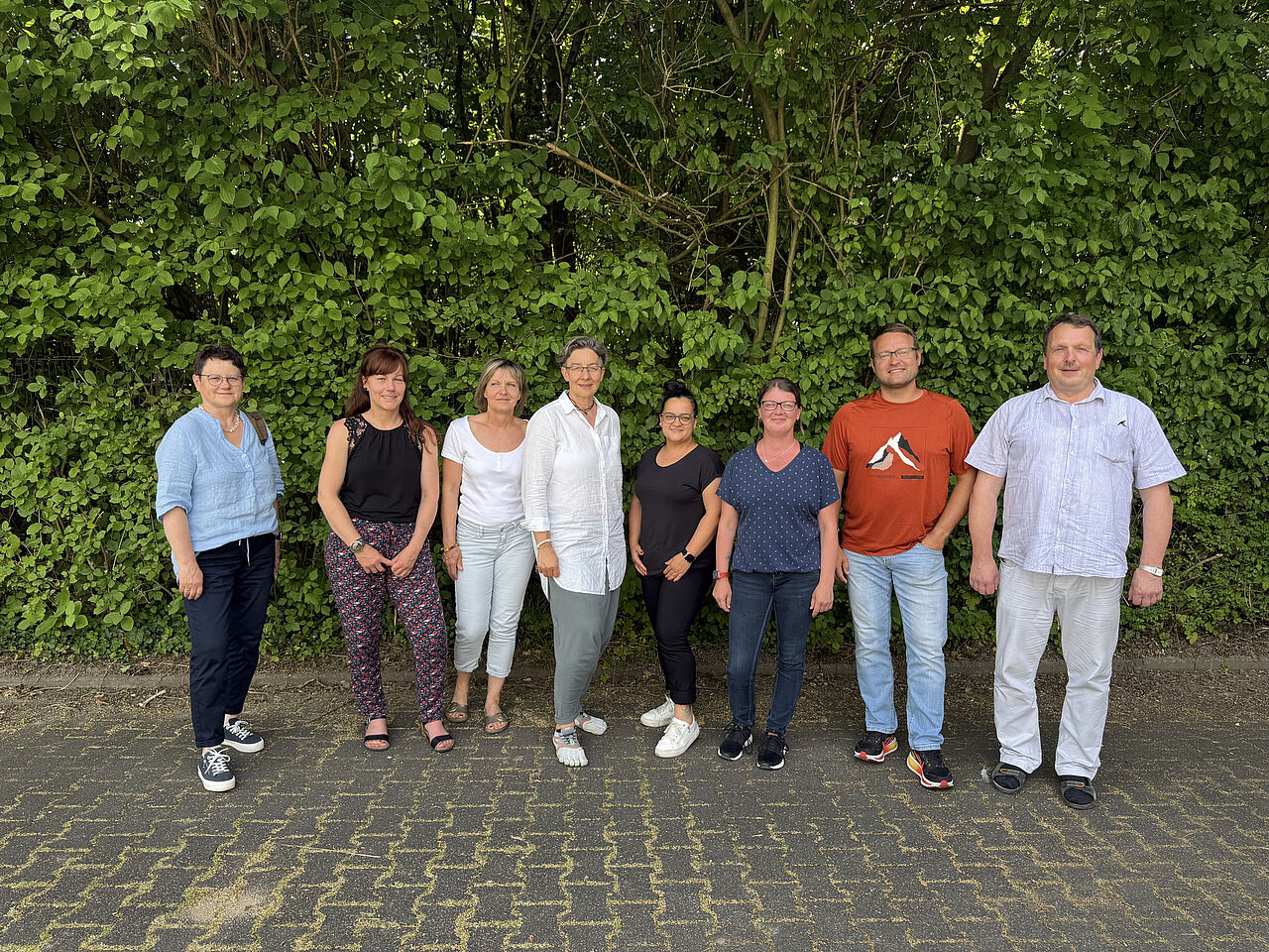 Acht Teilnehmende stehen bei sonnigem Wetter für ein Gruppenbild vor einer grünen Hecke.