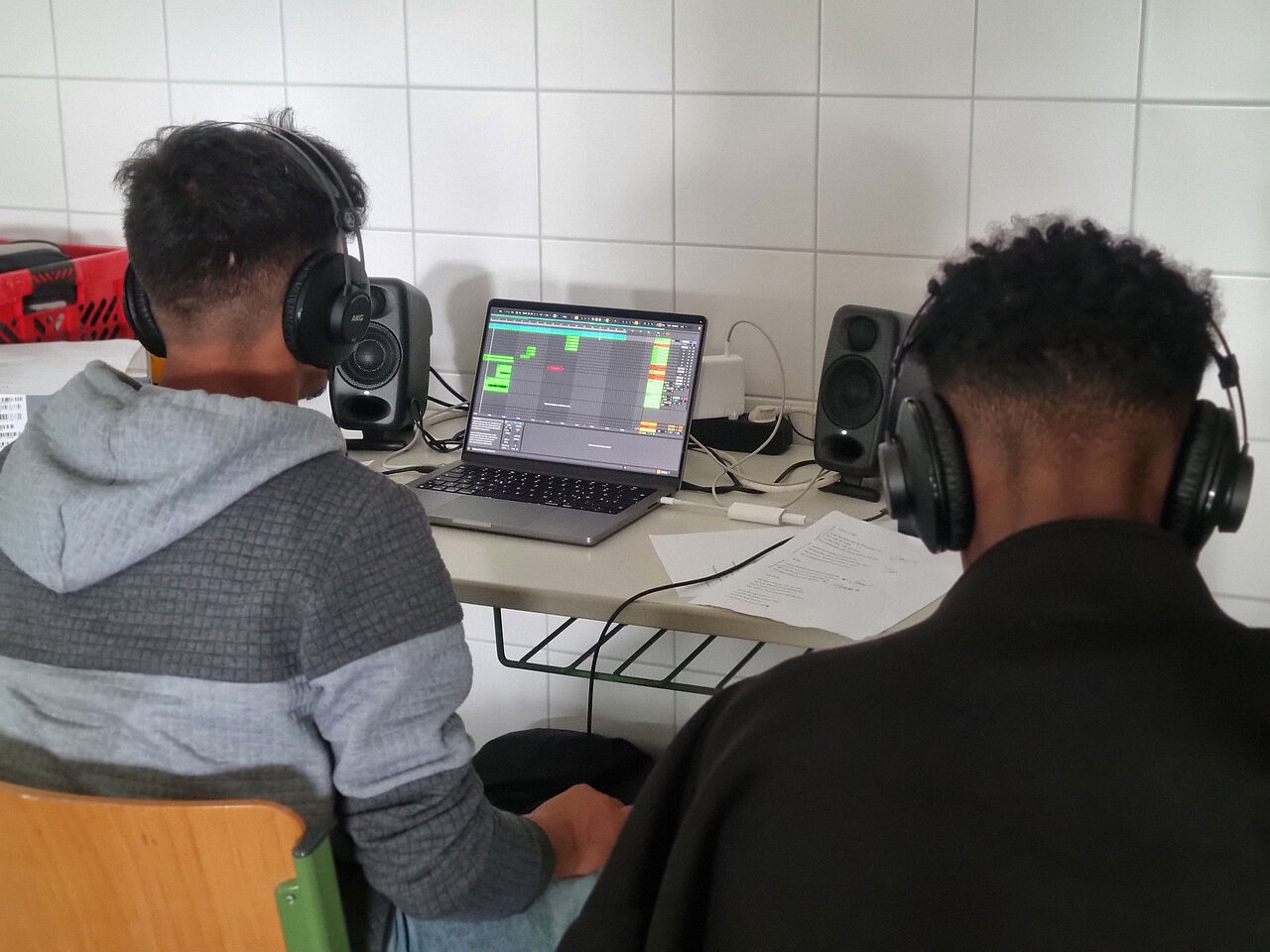Zwei Schüler hören über Kopfhörer eine Aufnahme ab und bearbeiten die Schulhymne gemeinsam am Laptop.