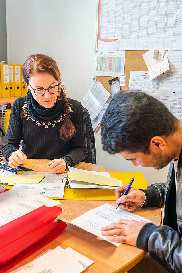 Eine Sozialpädagogin unterstützt einen Schüler beim Ausfüllen von Unterlagen in einem Beratungsgespräch.