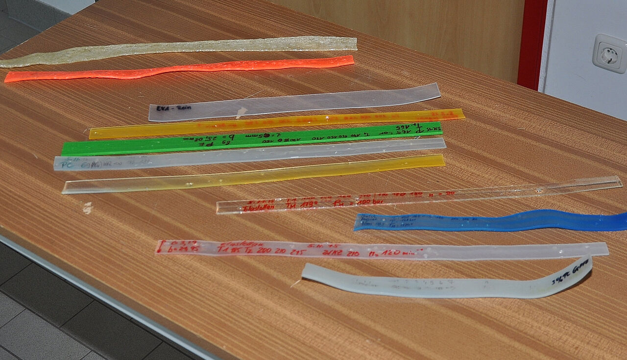 Verschiedenfarbige und beschriftete Kunststoff- und Elastomerproben liegen auf einem Arbeitstisch.