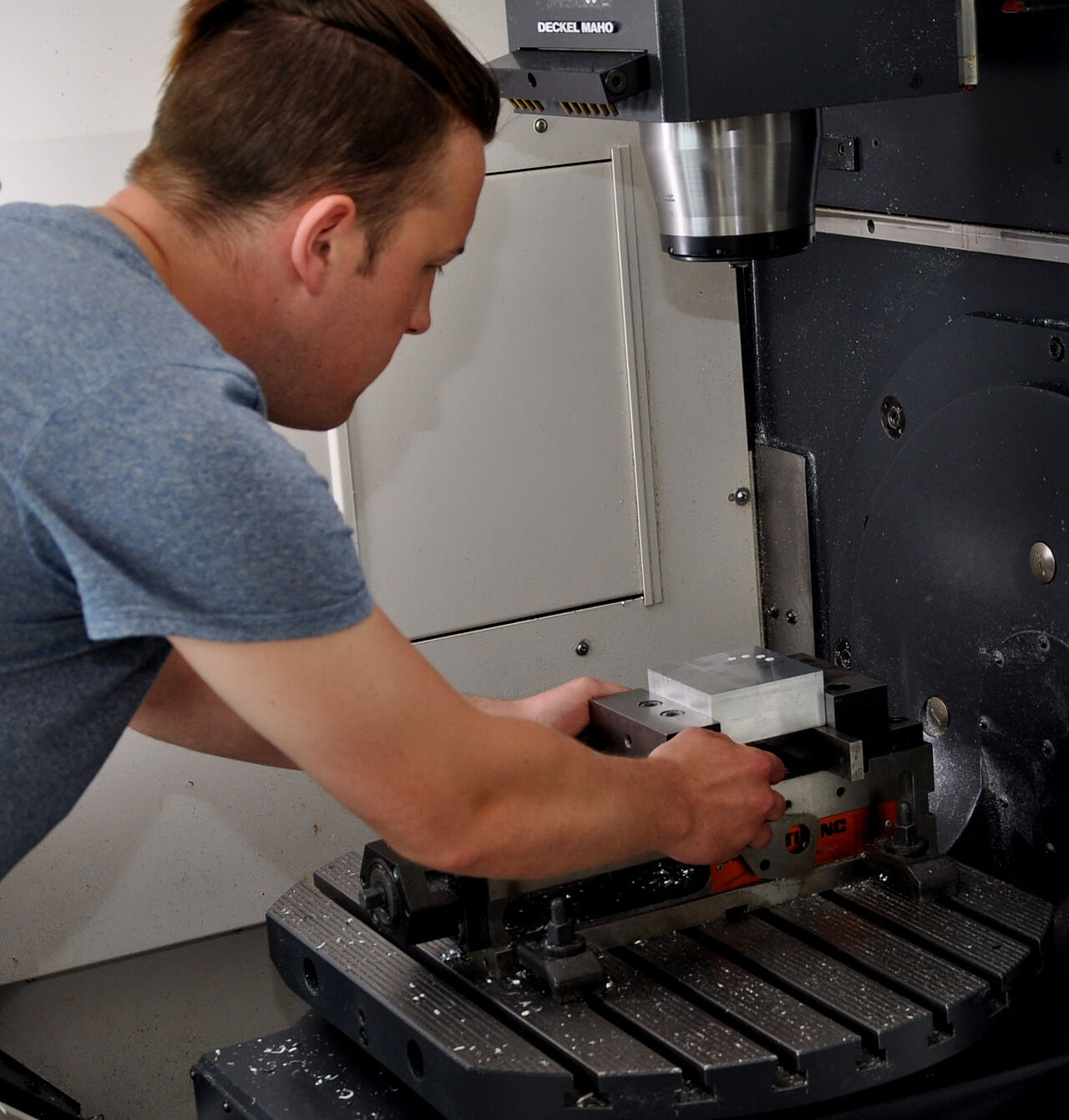 Ein Auszubildender richtet ein Metallwerkstück im Schraubstock einer CNC-Fräsmaschine aus.