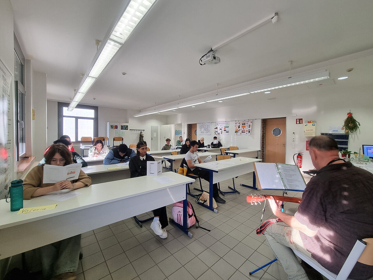 Schülerinnen und Schüler lesen die Liedblätter und singen gemeinsam zu einer Gitarrenbegleitung im Klassenraum.