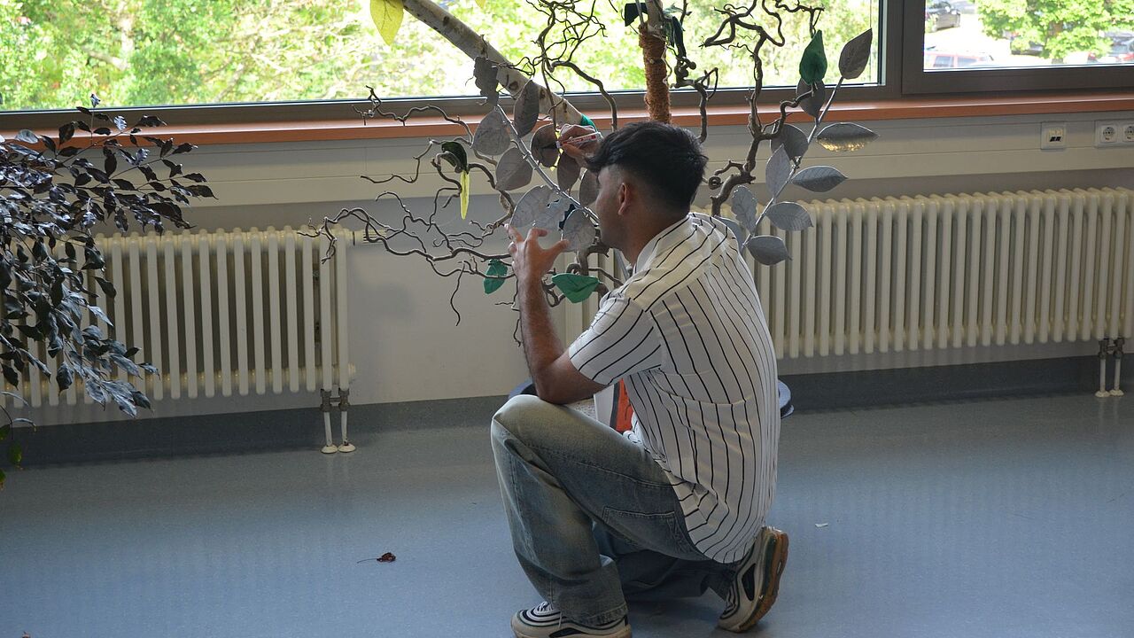 Ein Schüler verewigt seinen Namen auf dem gestalteten Projektbaum des Berufsvorbereitungsjahres.