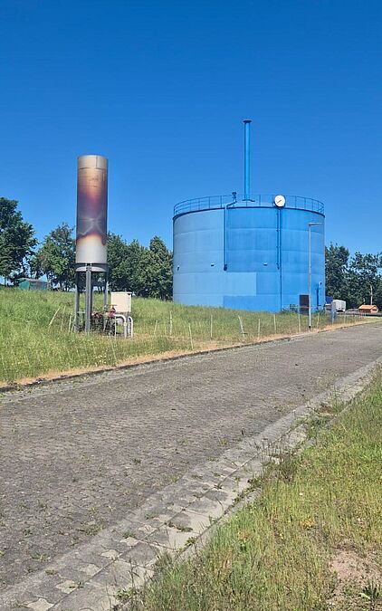Großer blauer Rundbehälter und eine hohe technische Säule auf dem Gelände der Kläranlage Gotha.