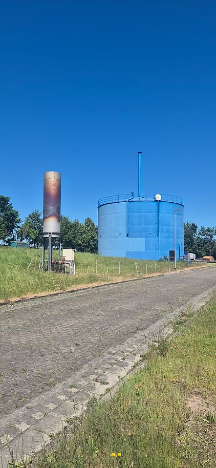 Großer blauer Rundbehälter und eine hohe technische Säule auf dem Gelände der Kläranlage Gotha.