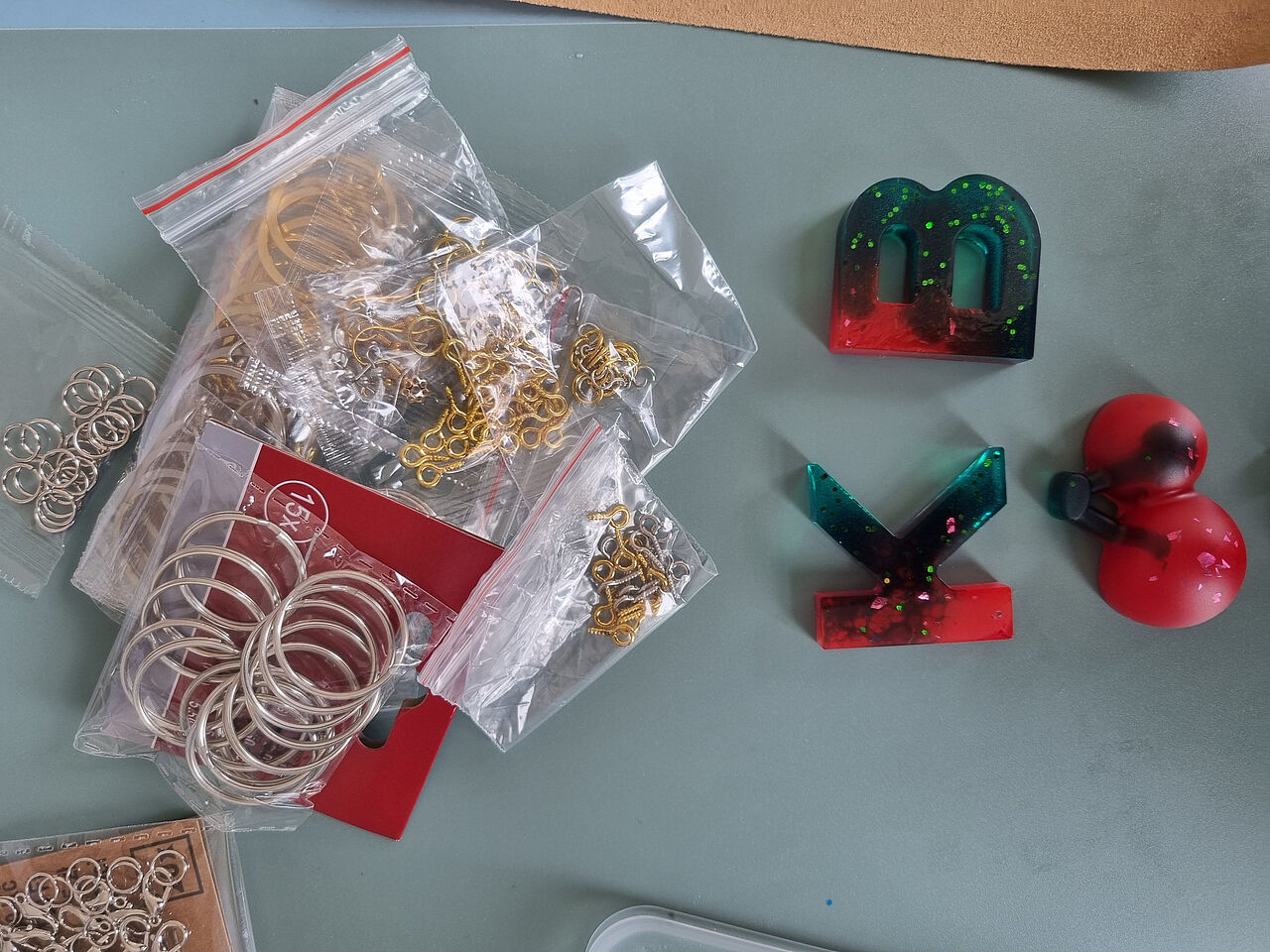 Gegossene Buchstaben und Anhänger aus mehrfarbigem Epoxidharz liegen neben Schlüsselringen und Befestigungsmaterial.