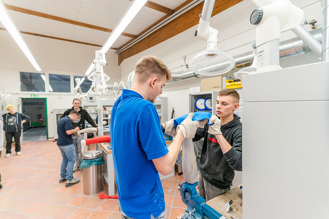 Zwei Auszubildende passen gemeinsam blaues Material an ein eingespanntes Unterschenkelmodell an.