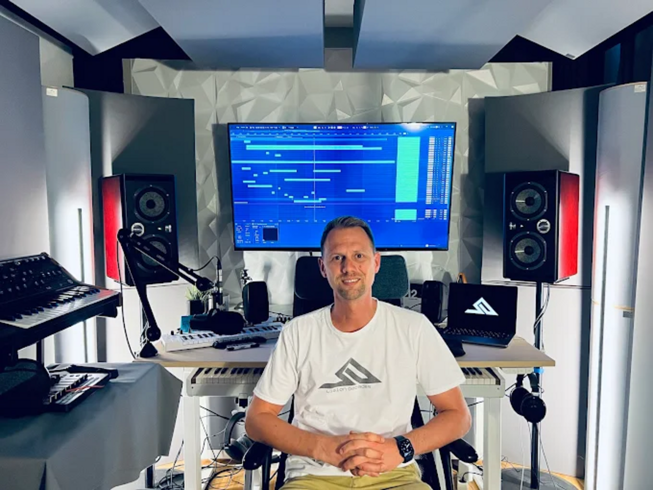 Projektbetreuer sitzt in einem professionell ausgestatteten Tonstudio vor Monitoren, Lautsprechern, Mikrofonen und Musikinstrumenten.