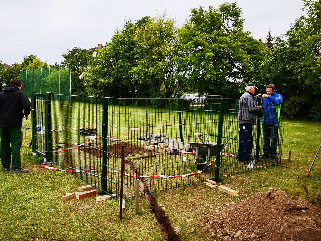 Projektbeteiligte errichten auf einer Grünfläche ein eingezäuntes Fundament für das Windrad.