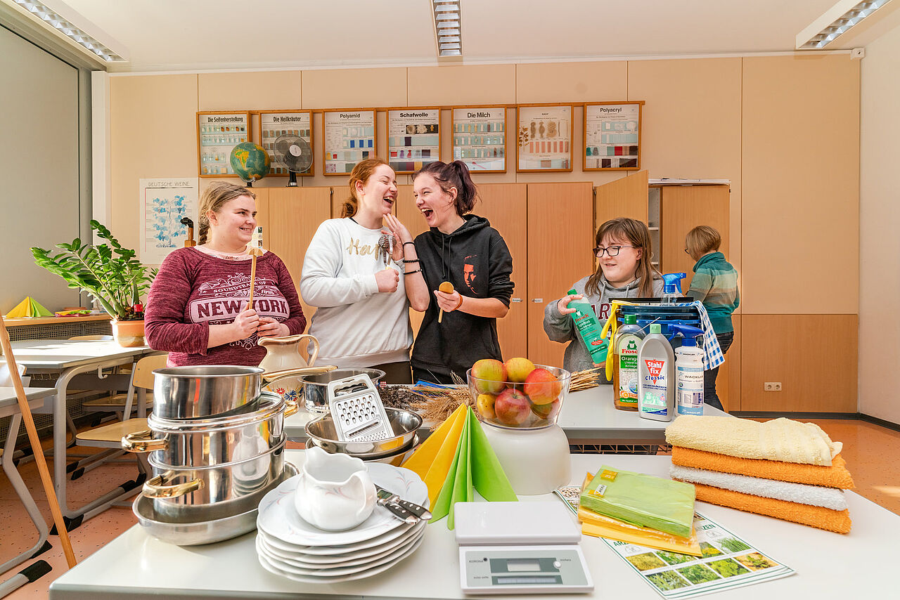 Schülerinnen der Förderberufsschule arbeiten mit Haushaltsutensilien, Reinigungsmitteln, Geschirr und Lebensmitteln im Fachraum Hauswirtschaft.