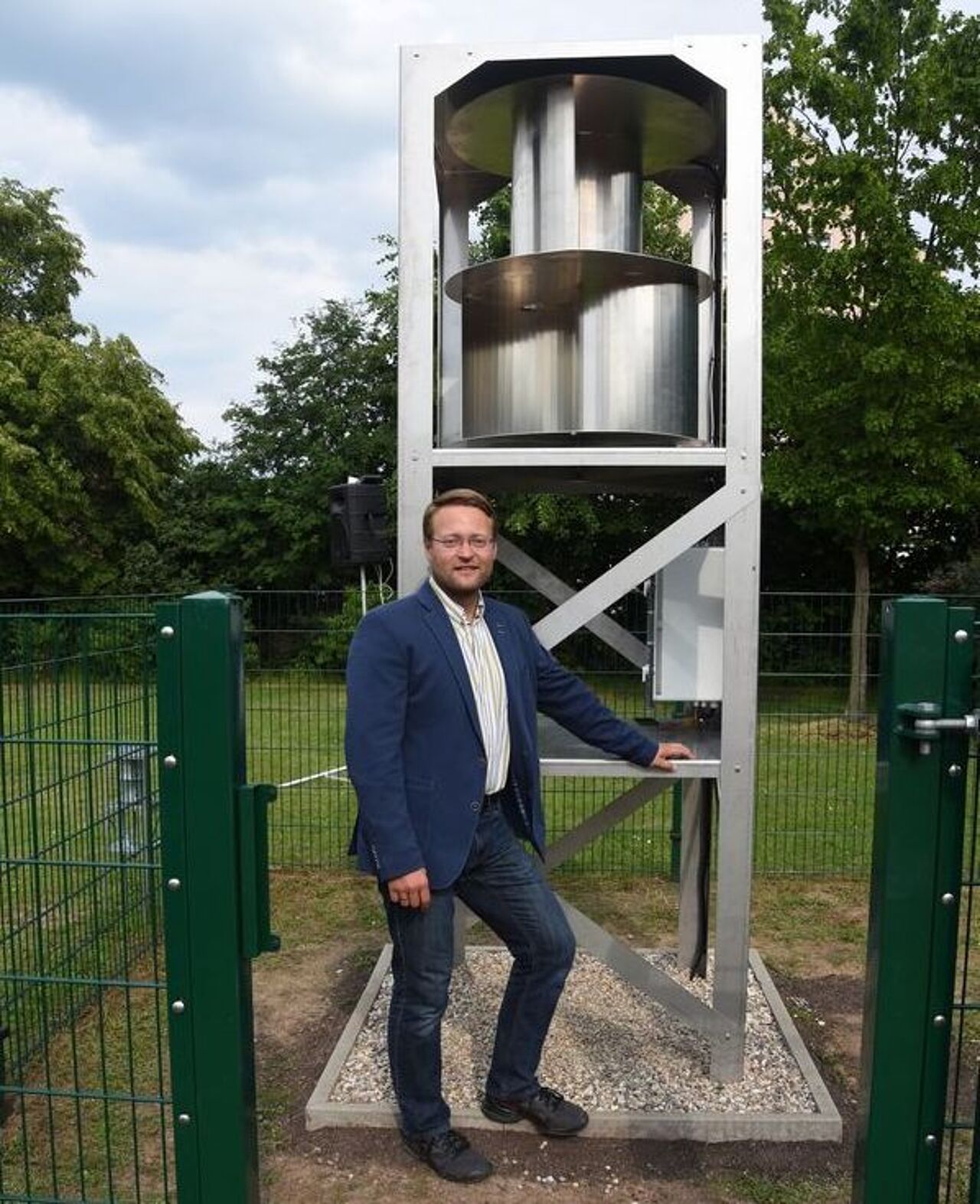 Ein Projektbeteiligter steht neben einem vertikalen Windrad auf dem Außengelände des Berufsschulzentrums.