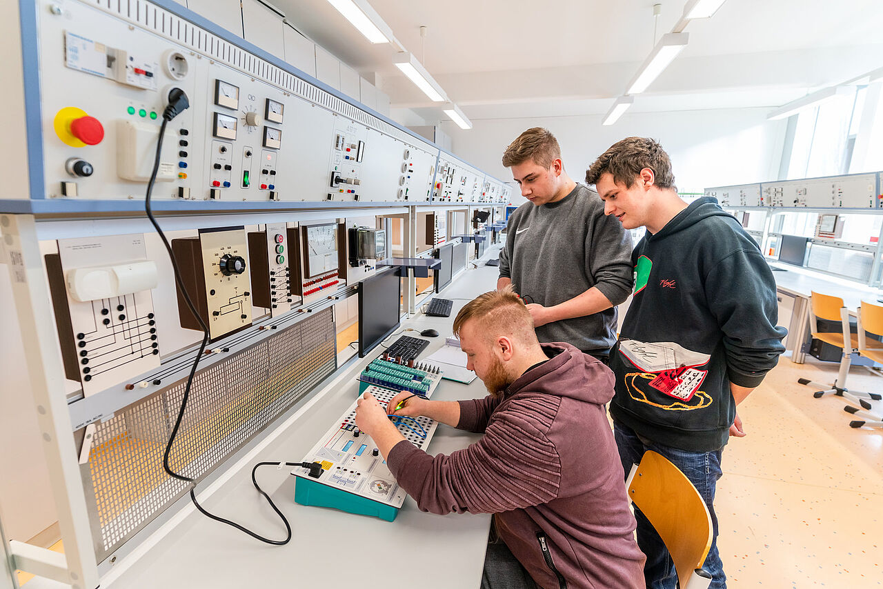 Drei Auszubildende arbeiten gemeinsam an einem elektrotechnischen Versuchsaufbau im Fachraum für Mechatronik.