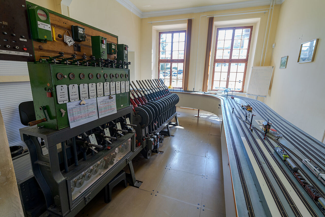 Mechanisches Stellwerk mit zahlreichen Hebeln neben einer großen Modelleisenbahnanlage.