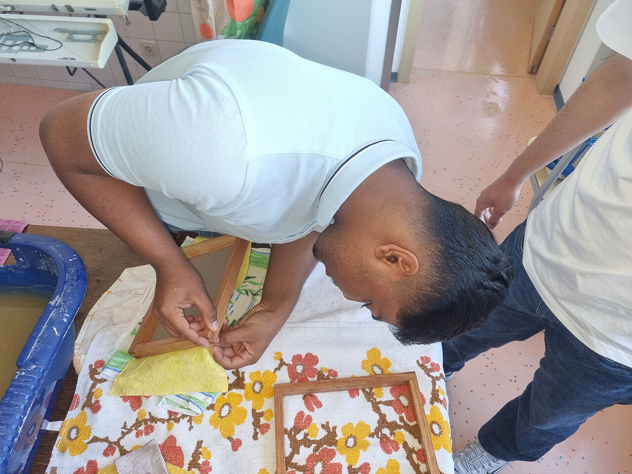 Ein Schüler löst vorsichtig ein handgeschöpftes Papierblatt aus einem Holzrahmen und legt es zum Trocknen auf ein Tuch.