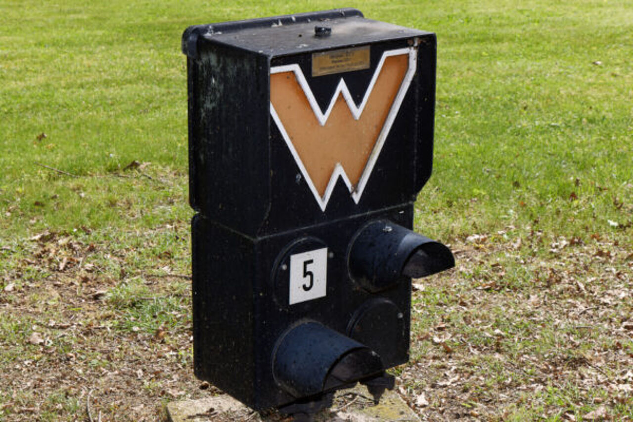 Historischer Signalschirm mit Warnzeichen und der Kennzeichnung „5“ auf einer Rasenfläche.