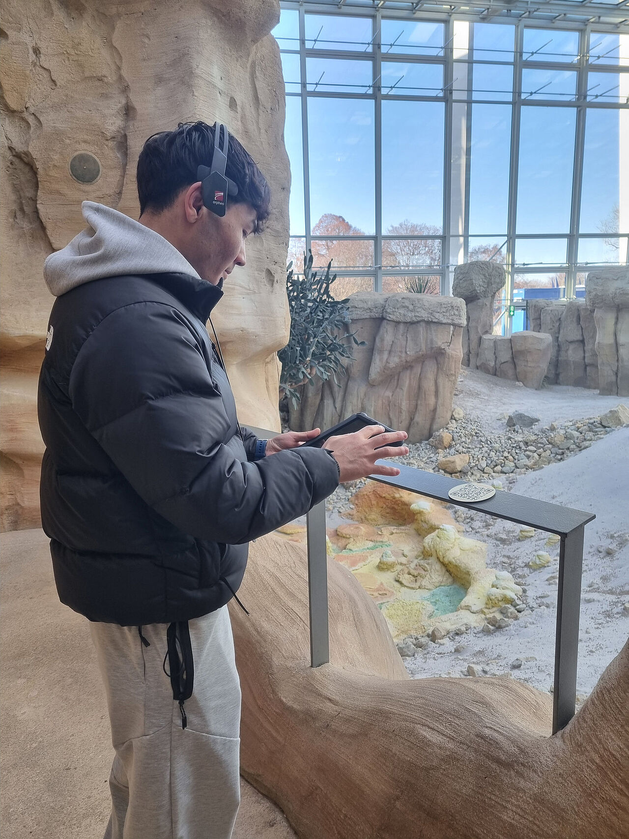 Ein Schüler nutzt Kopfhörer und ein mobiles Gerät an einer Hörstation in der Wüstenlandschaft des Grünen Klassenzimmers im egapark Erfurt.